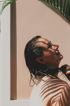 Portrait of a beautiful girl with bare shoulders without retouching with her natural imperfections. Above grows a green branch of the Howe palm tree. Palm tree gives a clear shadowの写真素材