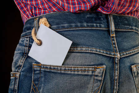 Gray cardboard label sticking out in the back pocket of fashionable blue jeans close-up