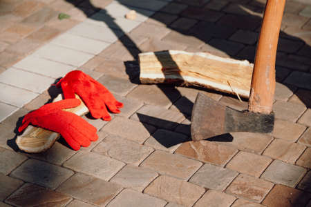 ax casts a shadow on the paving slabs in the yard. Nearby lies a chopped log and red work gloves