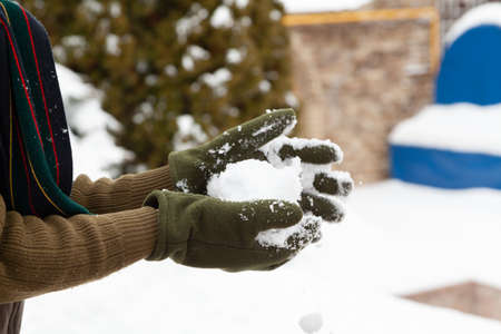 Winter fun. Hands in green fleece gloves form snowballs on a frosty day close-up