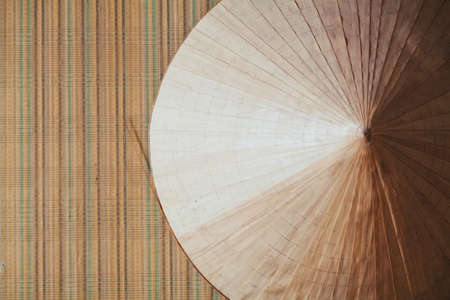 Asian conical hat made of palm leaves weighs right on the wall with vertical stripes on wallpaperの写真素材