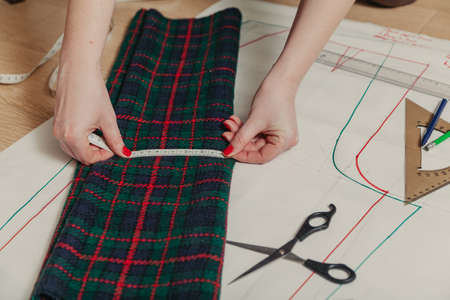 Designer creates a model. Female hands with manicure make markings on a piece of Scottish fabric...