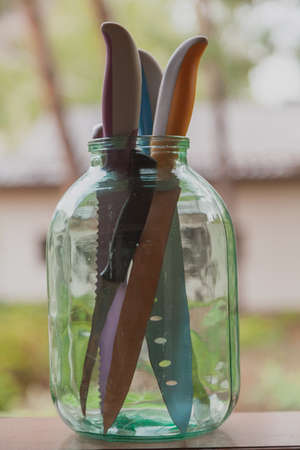 Jar knives. A group of kitchen knives of various sizes and shapes are in a large glass container on...