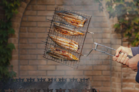 Cooking fish on the grill. Hands turn over metal grill with fish