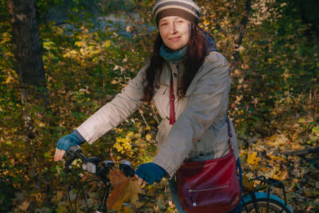 beautiful young woman in a beret with long red hair is standing with a bicycle in the middle of an...