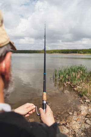 Fisherman holding a spinning rod with a reel against a background of white clouds against a blue sky