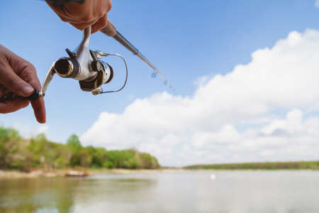 Fisherman holding a spinning rod with a reel against a background of white clouds against a blue sky