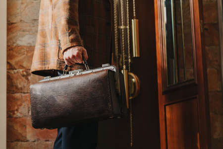 master watchmaker stands in front of an antique grandfather clock. Holds a valise with tools in his handの写真素材