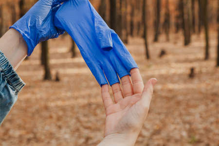 Prevention of infection. Man takes off blue rubber latex disposable gloves in autumn forest close upの写真素材