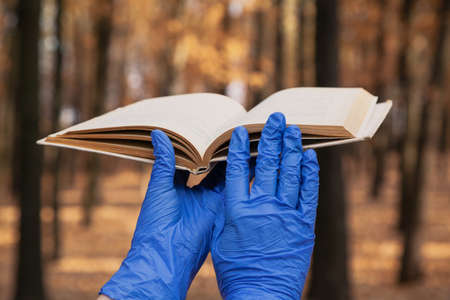 Reading in isolation. Hands in blue rubber latex disposable gloves hold an open book in the autumn...