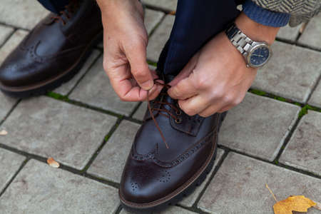 Hands tie a thin lace on a stylish left brogue shoe in autumn park close-up