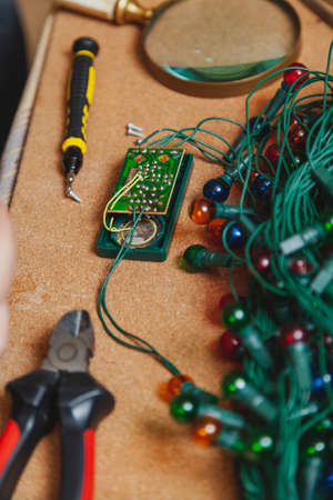 Repair of Christmas electric garland. On the table is an open control unit with microchips. Near the nippers and a screwdriver. Next lies a round magnifying glassの写真素材