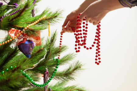 We decorate the Christmas tree. Hands hang a red garland of small balls on a green spruce branch close-upの写真素材