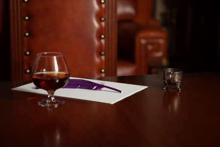 Poet inspiration kit. A glass goblet with brandy and an inkwell stands on a polished table. Nearby...