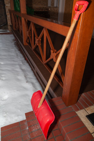 red snow shovel stands on red brick steps. In the background a wooden verandaの写真素材
