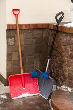 red and gray snow shovel stands in the corner of a stone fenceの写真素材