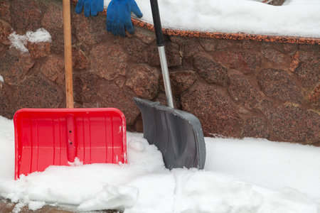 Snow cleaning tool. Red and gray plastic snow shovel stand in front of a stone fenceの写真素材