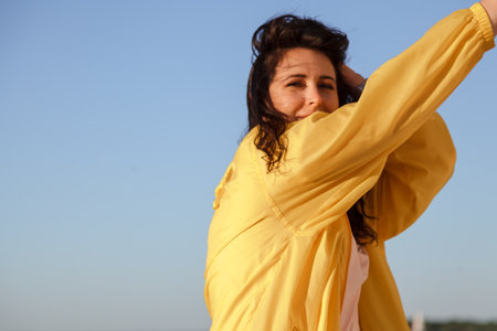 Portrait of a pretty plus size girl with long red hair and a bright yellow jacket against a blue skyの写真素材
