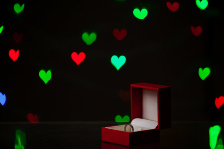 Valentine's Day gift. A silver ring stands in a red box on a dark background with multicolored heartsの写真素材