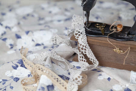 Vintage manual sewing machine and a skein of thread on a white fabric background with a blue pattern close-up. Braid and scissors lie nearbyの写真素材
