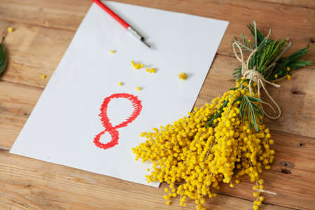 Eighth of March is a women's holiday. On a white sheet of paper, the number 8 is drawn in red. On the right is a bouquet of yellow mimosa. Nearby lies a vintage fountain penの写真素材