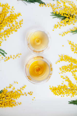 March 8 is a spring holiday. The number 8 is formed from two glasses of cognac on a white background close-up. A branch of yellow mimosa lies nearby. View from aboveの写真素材