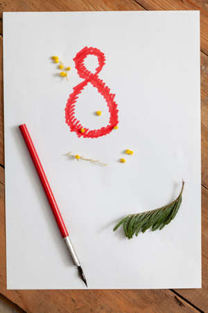 March 8 women holiday. Red number eight is drawn close-up on a white background. Nearby lies a vintage fountain pen and green mimosa leavesの写真素材