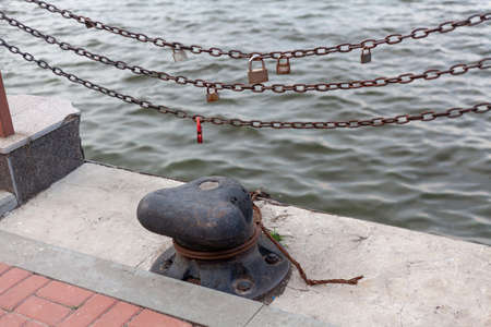 single cast iron bollard on a concrete dock. Three metal chains with commemorative locks hang over...