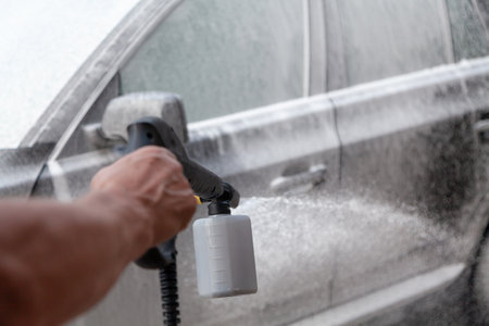 car is covered with white foam. Hand sprays detergent with a plastic high pressure washer gunの写真素材