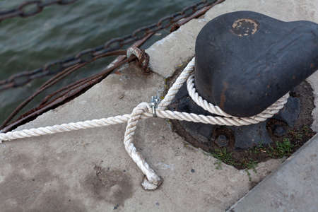 single cast iron bollard on a concrete dock. There is a white rope on the curbstone. View from above