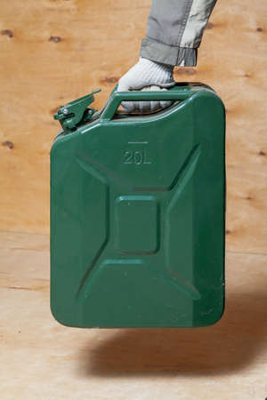 hand in a work glove holds a green metal canister on a light plywood backgroundの写真素材