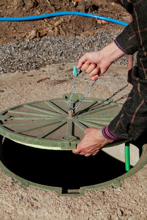 Hand pulls the metal chain on a round manhole cover close-up