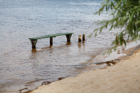 A flooded shop. The water level in the river rose sharply and flooded the sandy beach. Green wooden bench stands in the waterの写真素材