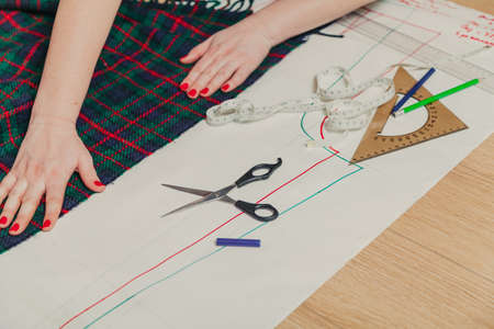 Designer creates a model. Female hands with a manicure make markings on a piece of Scottish fabricの写真素材