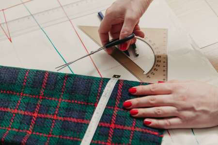 Designer creates a model. Female hands with a manicure make markings on a piece of Scottish fabricの写真素材