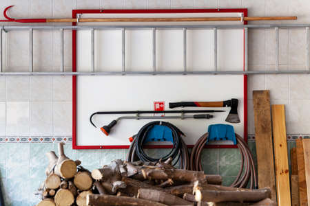 Fire safety corner. On the wall hangs a white shield on which hangs an ax, a hook, a hose and an...