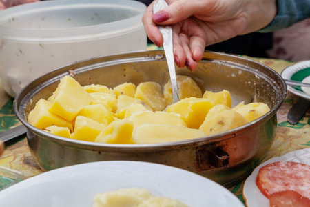 Woman hand with manicure lays boiled potatoes from a round metal plate close-up
