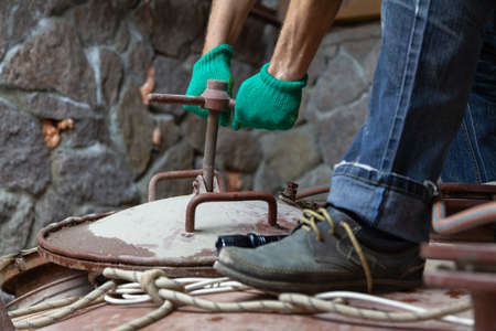 Hands in green protective gloves, twist the metal hatch bracket with a screw lock on top of a large capacityの写真素材