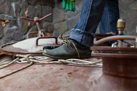 foot of the fitter in the boot stands on top of a large metal container. Close to the hatch with...