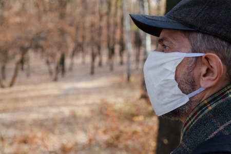 Portrait of a man in a white mask. A man in a cap and a white medical mask stands in a spring forestの写真素材