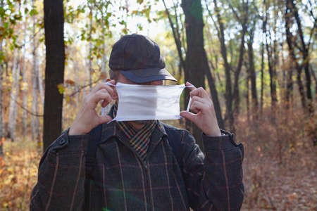 man in a cap puts on a white medical mask in a spring forestの写真素材