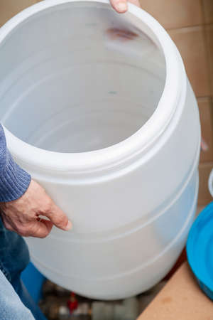 Plumber hands hold a round plastic water tank for osmosis water purification system
