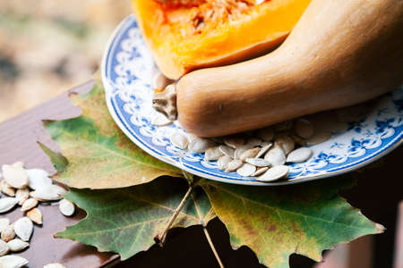 Autumn still life. An elongated pumpkin and white seeds lie on a plate. Maple leaves lie on a wooden railingの写真素材
