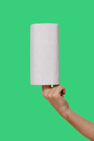 roll of white paper towels is held vertically on the fingers of the right hand isolated on green...