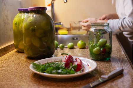 Preservation of green tomatoes. Two jars of canned green tomatoes stand on a granite countertop. Nearby is a small jar of tomatoes without pickleの写真素材