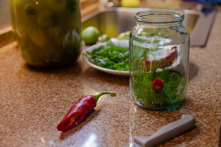 Preparation for preserving vegetables. A glass jar with green dill leaves stands on the table top....