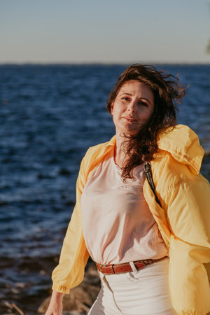 Nice plus size girl with long red hair is standing on the background of a water surface. Portrait of...