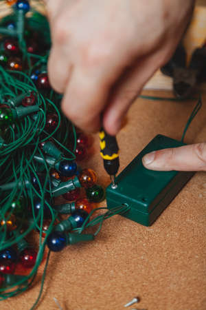 Preparing for the New Year. Repair of a Christmas tree electric garland. Hands open the control box box with a screwdriverの写真素材