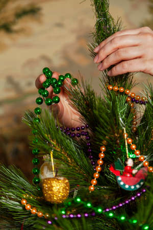 We decorate the Christmas tree. Hands hang a green garland of small balls on a green spruce branch close-upの写真素材