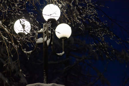 Evening street lighting. Three retro-style circular outdoor lights provide a beautiful white light. There is snow on topの写真素材